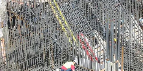 Operaio lavora su un'impalcatura di ferro per il cemento armato. La sua presenza suggerisce la cura necessaria per garantire la durata del cemento armato.