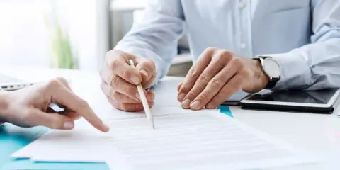 Due mani esaminano un documento, una indica un punto mentre l'altra tiene una matita, forse per la dichiarazione di inizio attività.