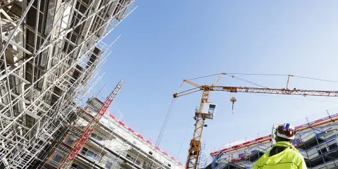 Operaio con giubbotto alta visibilità osserva un cantiere edile con gru e impalcature. Capire cassa edile come funziona è fondamentale per la sicurezza.