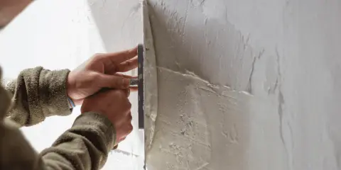 Mani esperte creano una finitura a frattazzo su un muro grezzo, dando forma alla texture.