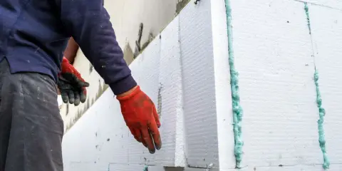 Installazione di un cappotto termico su intonaco esistente. Pannelli in polistirene espanso vengono fissati con schiuma espansa.