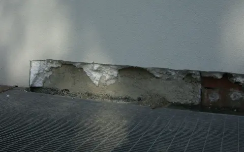 Dettaglio di un muro con isolamento danneggiato, mostrando la differenza tra xps e eps. Grata metallica in primo piano.
