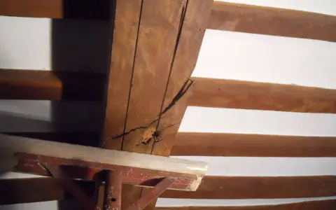 Dettaglio di travi in legno con crepe, in attesa di consolidamento. Supporto metallico provvisorio.
