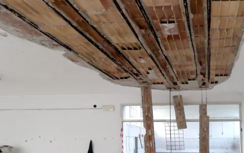 Solaio imbarcato con travi in laterizio a vista e armature metalliche. Caduta di calcinacci e pilastri in mattoni parzialmente distrutti.