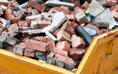 Cumulo di mattoni rotti e detriti edili in un cassone giallo. Questo è il materiale di risulta, scarti di demolizione pronti per lo smaltimento.