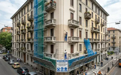 Lavoratori in azione per dipingere casa esterno, con impalcature e teli blu che coprono la facciata in ristrutturazione.