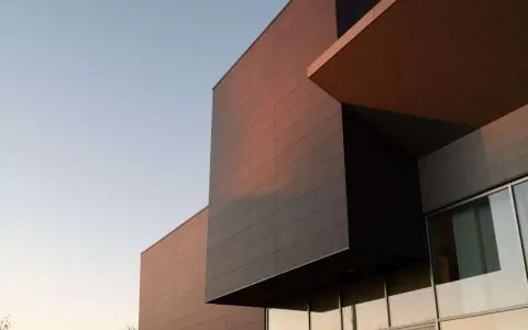 Edificio moderno con facciata ventilata in pannelli scuri e color rame, illuminato dalla luce del tramonto.