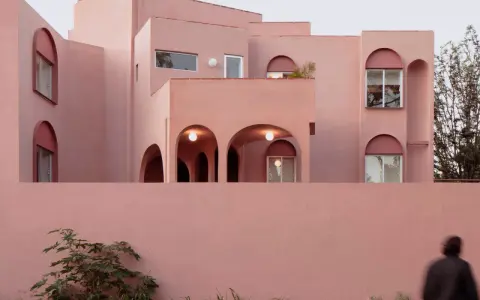 Edificio moderno con un particolare colore intonaco esterno rosa cipria. Archi e finestre a tutto sesto creano un gioco di luci e ombre.