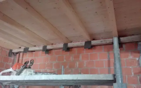 Travetti in legno per solaio, con staffe metalliche fissate a un muro di mattoni. L'interasse travetti solaio è visibile.