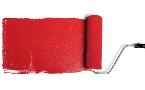 Rullo da pittura stende una striscia di vernice rosso antico, ideale per il colore esterno di una casa.