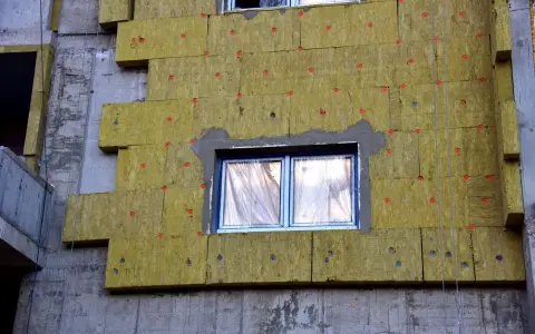 Iniziano i lavori per fare il cappotto alla casa: pannelli isolanti gialli fissati al muro grezzo, con finestre protette.