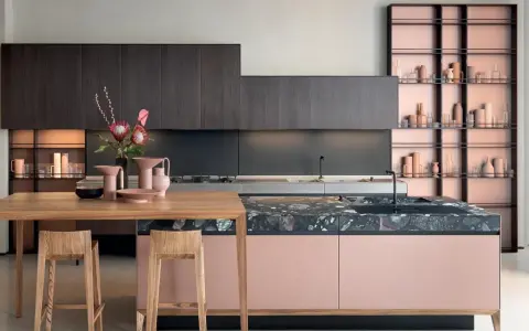 Cucine moderne con un mix di colori audaci: ante rosa cipria, top in marmo scuro e scaffalature color rame.