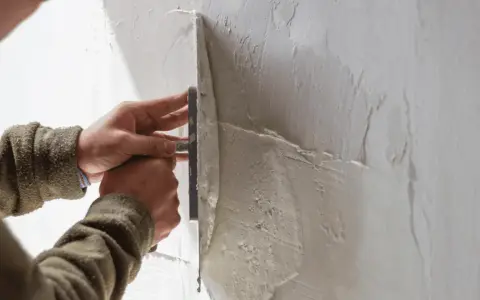 Mani esperte creano una finitura a frattazzo su un muro grezzo, dando forma alla texture.