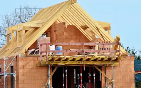 Costruzione di una casa in mattoni con tetto in legno. La struttura è in fase avanzata, con un **durc di congruità** verificato per i lavori in corso.