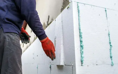 Installazione di un cappotto termico su intonaco esistente. Pannelli in polistirene espanso vengono fissati con schiuma espansa.