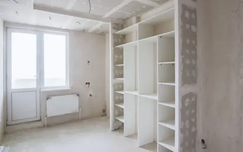 Un armadio bianco con ripiani è in fase di installazione. Sopra l'armadio, si intravede il cartongesso del soffitto, in attesa di finitura.