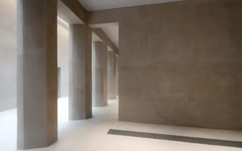 Colonnato moderno con pareti e pilastri in intonaco o stucco color sabbia, illuminato da luce soffusa.