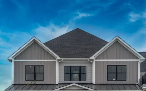 La facciata di una casa moderna con un elegante colore esterno casa tortora scuro, finestre nere e un tetto scuro sotto un cielo blu intenso.