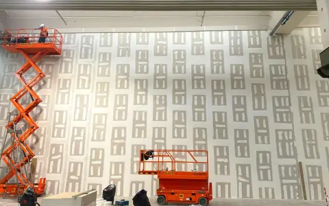 Lavori in corso su una parete con pannelli di cartongesso rei. Due piattaforme aeree arancioni sono posizionate per raggiungere l'altezza.