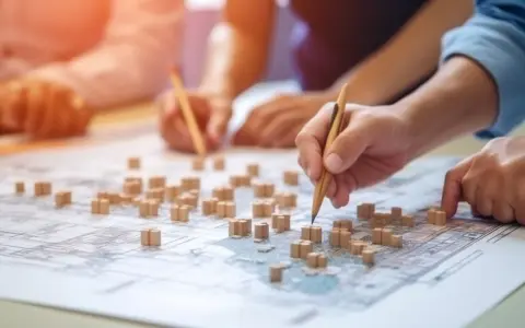 Mani che studiano una mappa con modelli di edifici, per capire cosa sono gli standard urbanistici e come definire lo sviluppo di una città.