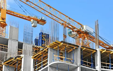 Cantiere edile con gru gialla e strutture in cemento armato. Si nota il puntellamento solaio con supporti blu e tavole di legno.