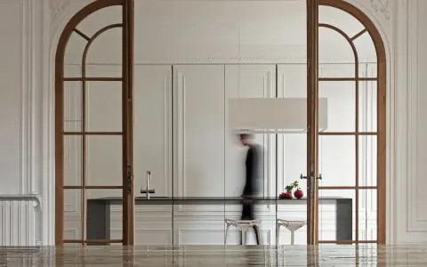 Archi interni casa con porte in legno che incorniciano una cucina moderna. Una figura sfocata attraversa lo spazio.