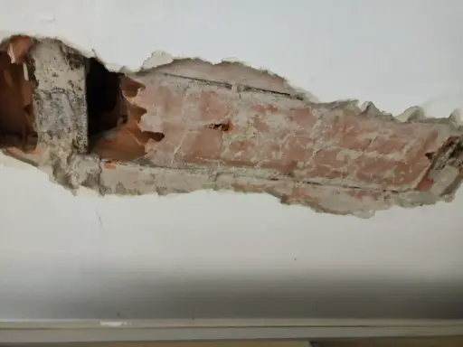 Intonaco danneggiato rivela l'intradosso del solaio con mattoni a vista e travi in legno.