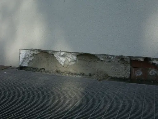 Dettaglio di un muro con isolamento danneggiato, mostrando la differenza tra xps e eps. Grata metallica in primo piano.