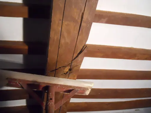 Dettaglio di travi in legno con crepe, in attesa di consolidamento. Supporto metallico provvisorio.