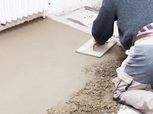 Operaio stende il massetto con una spatola, mostrando la differenza tra massetto e calcestruzzo grezzo.