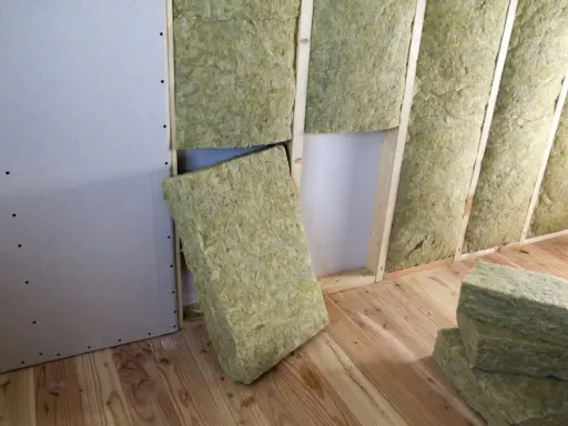 Pannelli di lana di roccia pronti per l'isolamento termico casa, inseriti tra le travi di legno di una parete in costruzione.