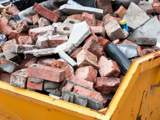 Cumulo di mattoni rotti e detriti edili in un cassone giallo. Questo è il materiale di risulta, scarti di demolizione pronti per lo smaltimento.