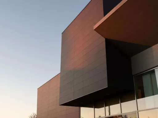 Edificio moderno con facciata ventilata in pannelli scuri e color rame, illuminato dalla luce del tramonto.