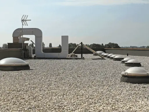 Tetto piano ricoperto di ghiaia, con lucernari a cupola e condotti di ventilazione. Il vespaio ghiaia protegge la copertura.