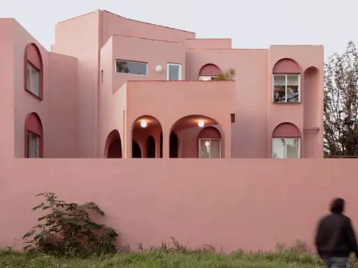 Edificio moderno con un particolare colore intonaco esterno rosa cipria. Archi e finestre a tutto sesto creano un gioco di luci e ombre.