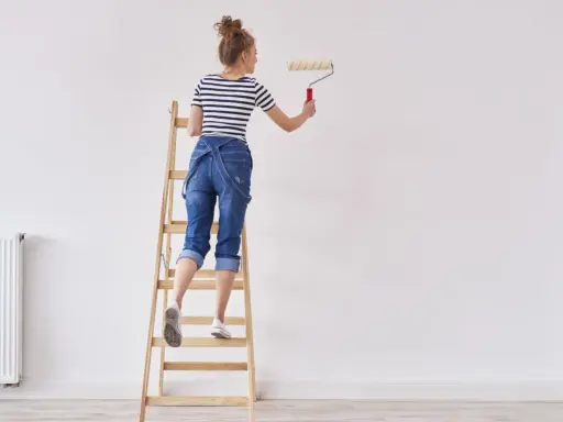 Donna su scala con rullo, pronta a tinteggiare le pareti di bianco.