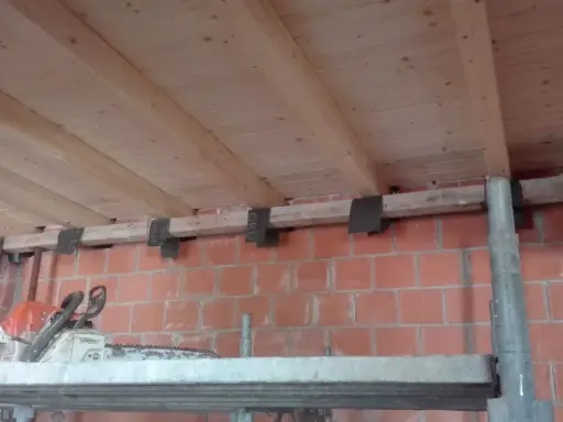 Travetti in legno per solaio, con staffe metalliche fissate a un muro di mattoni. L'interasse travetti solaio è visibile.