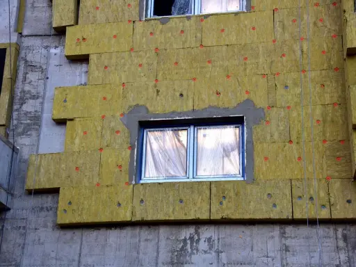 Iniziano i lavori per fare il cappotto alla casa: pannelli isolanti gialli fissati al muro grezzo, con finestre protette.