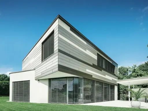 Moderna casa con pareti esterne a fasce grigie e bianche, grandi finestre con persiane e prato verde.