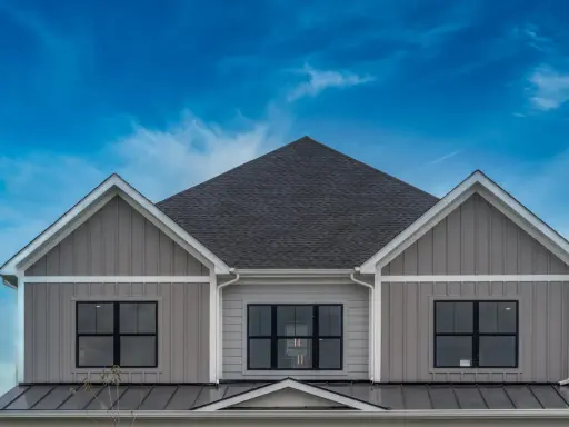 La facciata di una casa moderna con un elegante colore esterno casa tortora scuro, finestre nere e un tetto scuro sotto un cielo blu intenso.