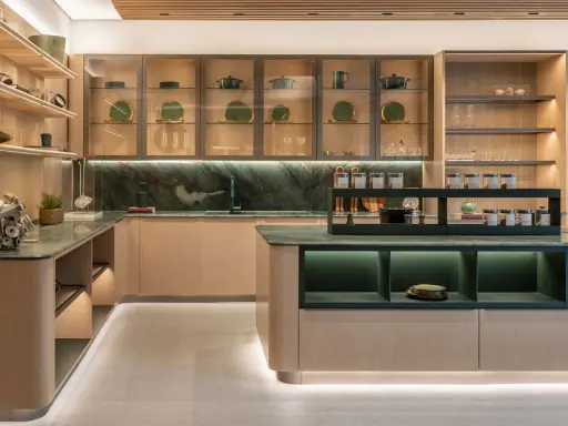 Una cucina moderna con un'isola centrale. Il piano di lavoro e il paraschizzi in marmo verde creano un contrasto elegante con le ante in legno chiaro. Il colore verde domina, donando un tocco di natura e raffinatezza.