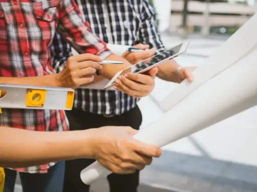 Team di operai esamina progetto su tablet, livella e rotoli di carta. Aggiornamento sal stato avanzamento lavori.