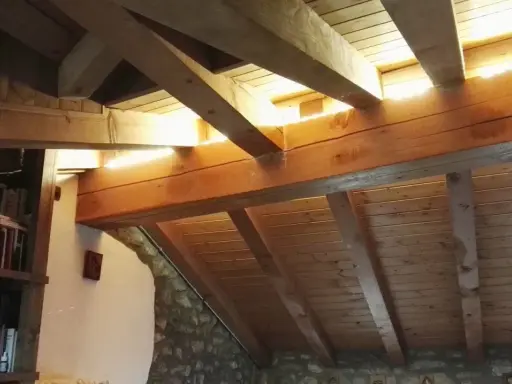 Soffitto in legno con travetti a vista, illuminato da luce naturale. Si nota una libreria e pareti in pietra. La lunghezza massima travetti solaio è ben visibile.