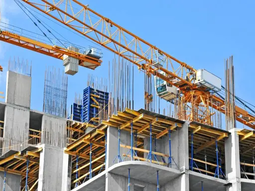 Cantiere edile con gru gialla e strutture in cemento armato. Si nota il puntellamento solaio con supporti blu e tavole di legno.