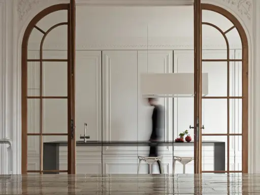Archi interni casa con porte in legno che incorniciano una cucina moderna. Una figura sfocata attraversa lo spazio.