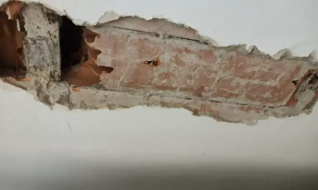 Intonaco danneggiato rivela l'intradosso del solaio con mattoni a vista e travi in legno.