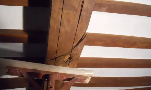 Dettaglio di travi in legno con crepe, in attesa di consolidamento. Supporto metallico provvisorio.