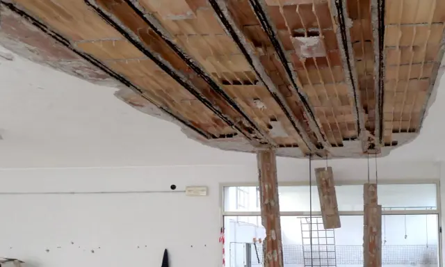Solaio imbarcato con travi in laterizio a vista e armature metalliche. Caduta di calcinacci e pilastri in mattoni parzialmente distrutti.