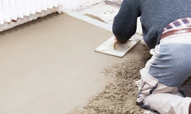 Operaio stende il massetto con una spatola, mostrando la differenza tra massetto e calcestruzzo grezzo.