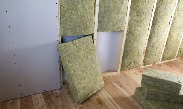 Pannelli di lana di roccia pronti per l'isolamento termico casa, inseriti tra le travi di legno di una parete in costruzione.